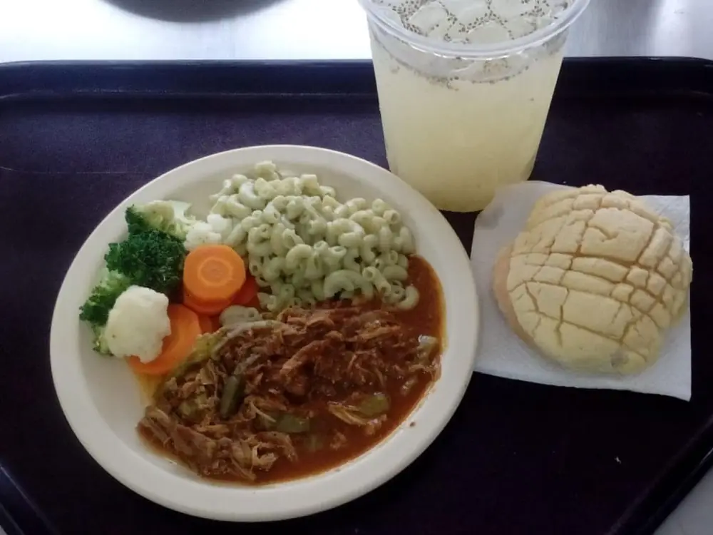 Charola servida con guisado, pasta, verduras, pan dulce y agua